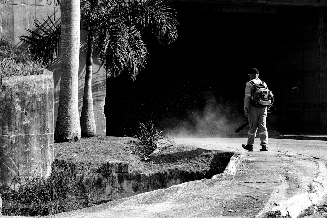 A lone worker uses a leaf blower to clear debris, creating a cloud of dust against a dark background.