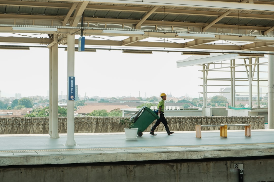 man-in-hard-hat-pulls-large-green-suitcase-on-platform-0uyfen-1kta